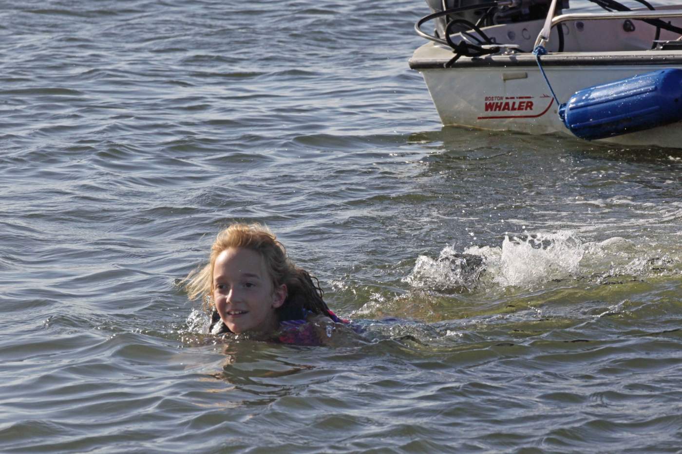 Young girl smiling swimming away from boat
