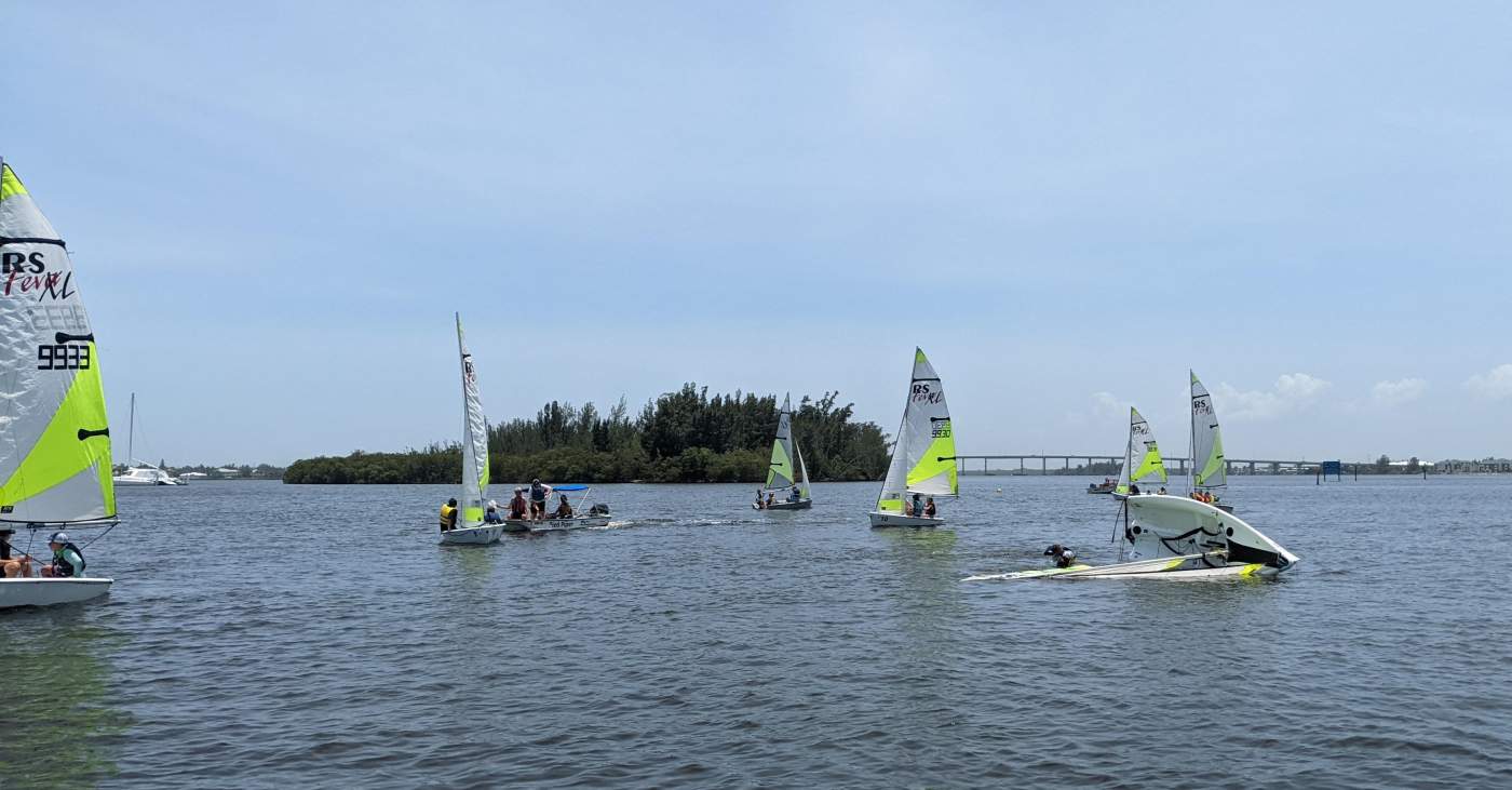 A group of sailboats surrounding another sailboat laying down on its side