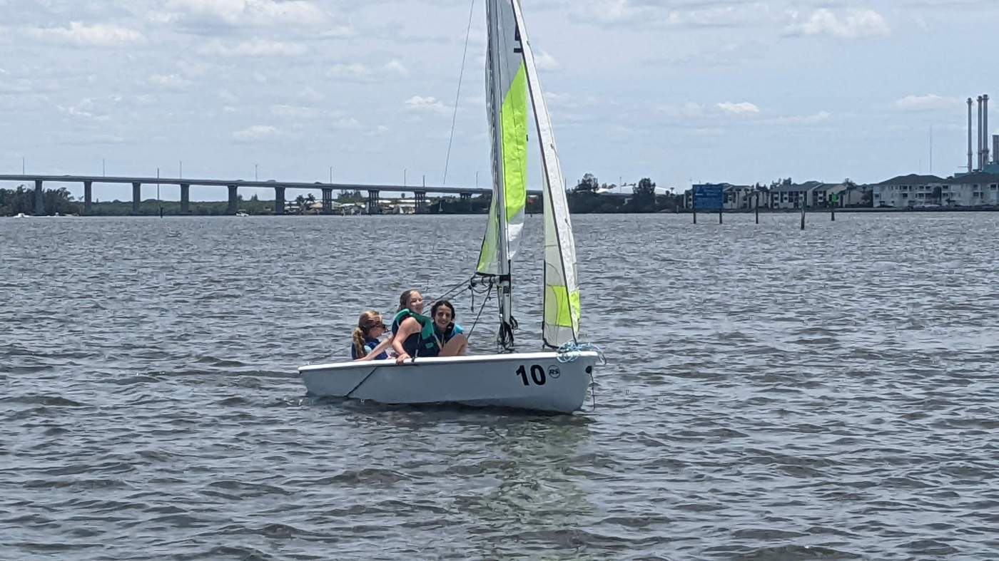 Three girls sailing a boat with a bridge in the background