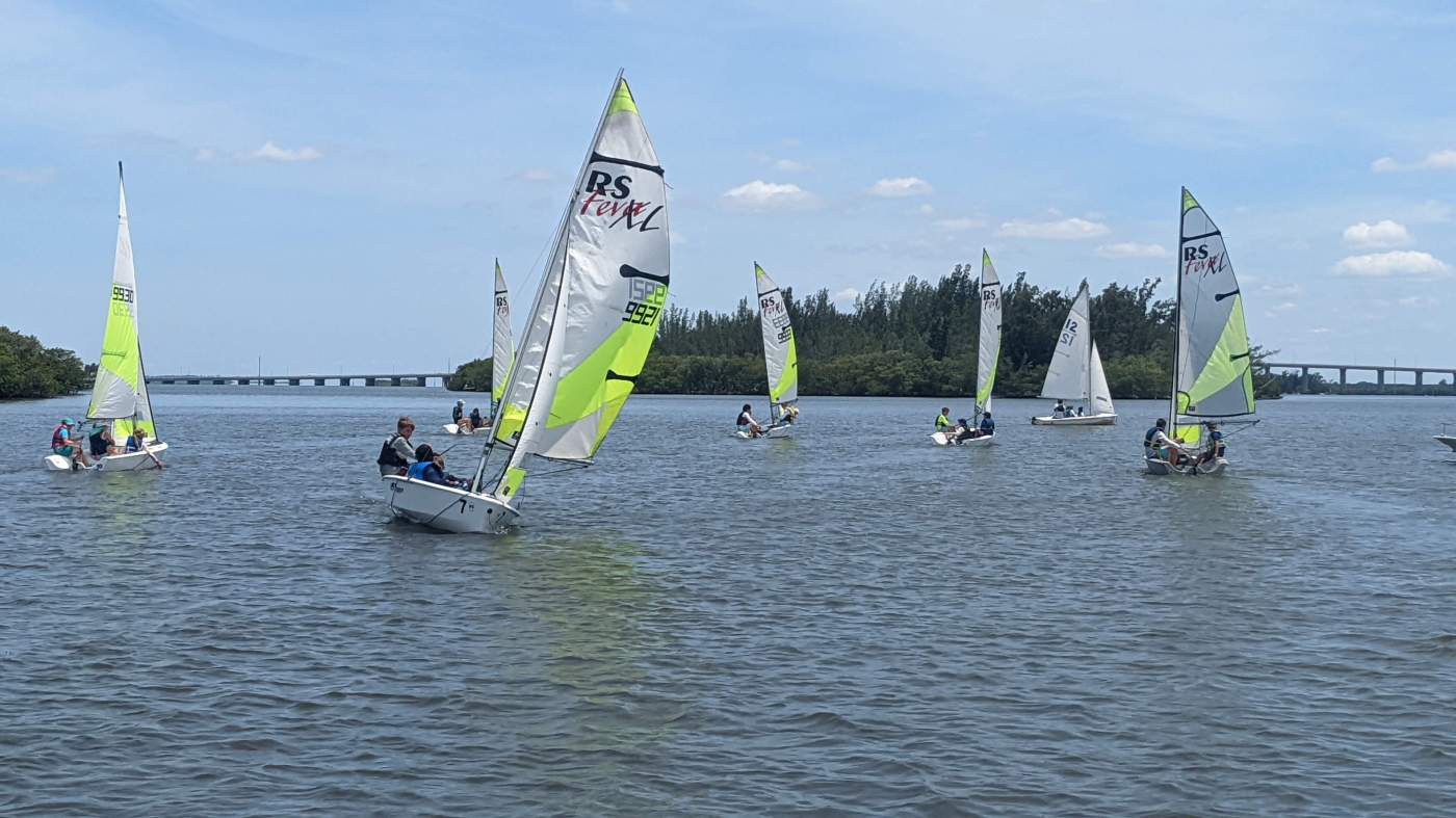A group of sailboats sailing in the lagoon with two bridges in the background