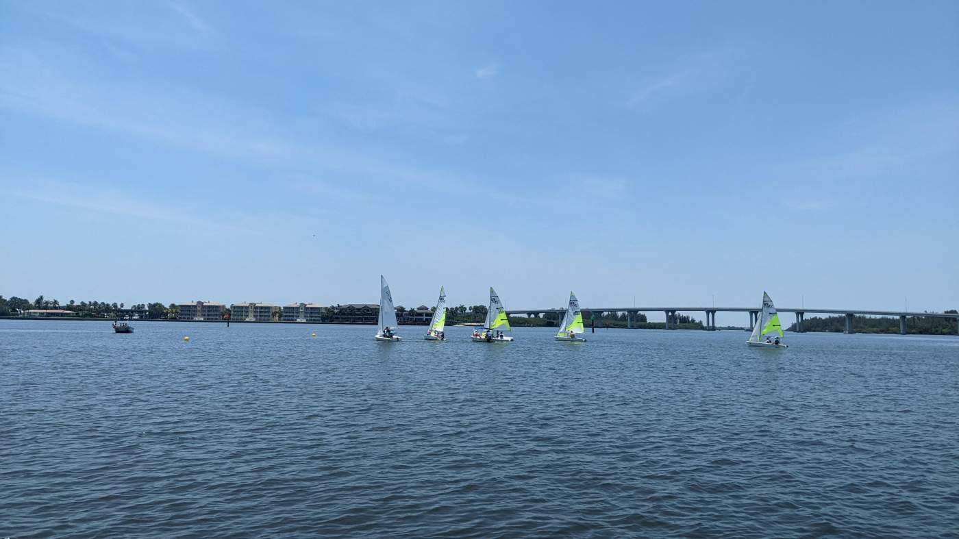 A group of sailboats sailing in the lagoon with a bridge in the background