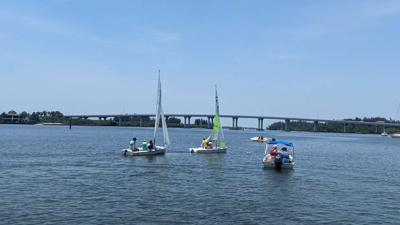 A group of sailboats sailing in the lagoon with a bridge in the background