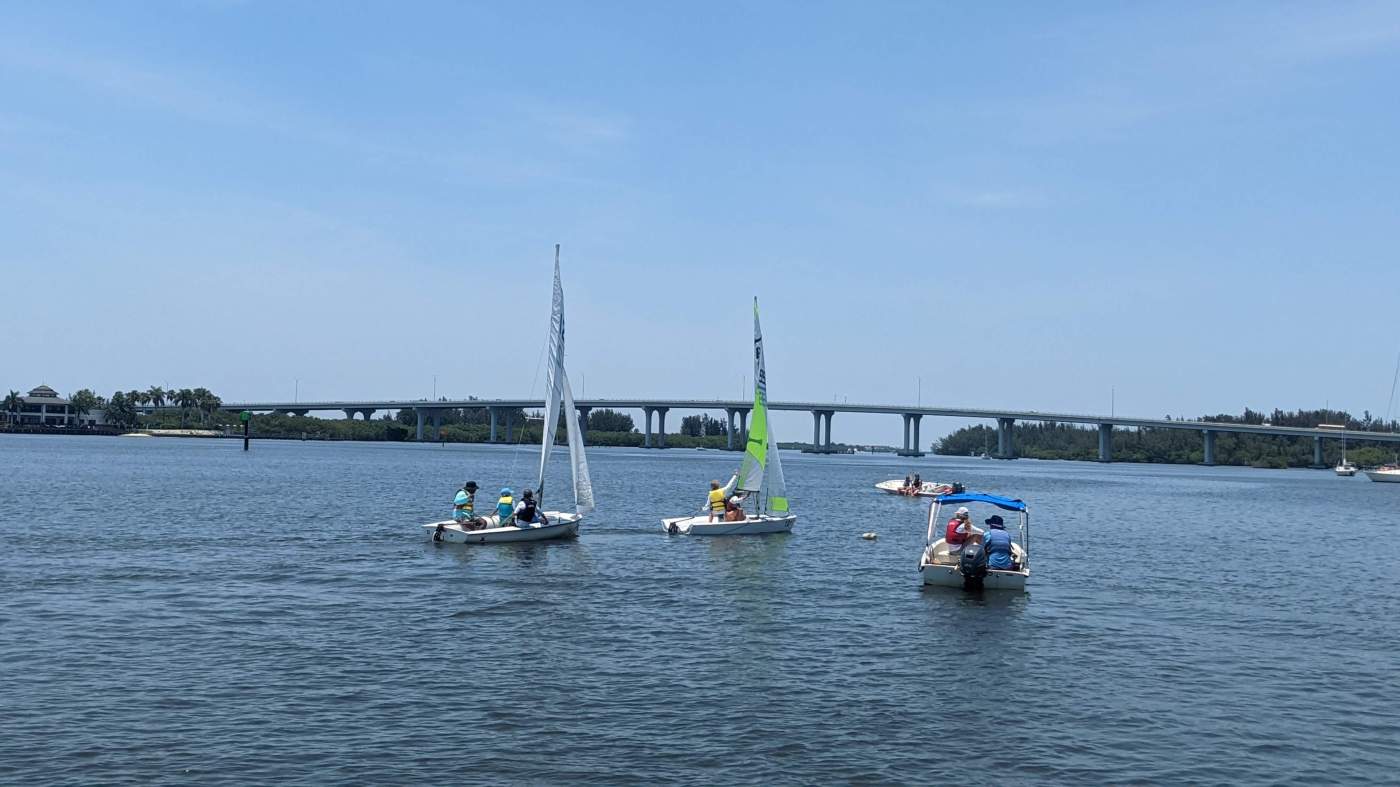 A group of sailboats sailing in the lagoon with a bridge in the background