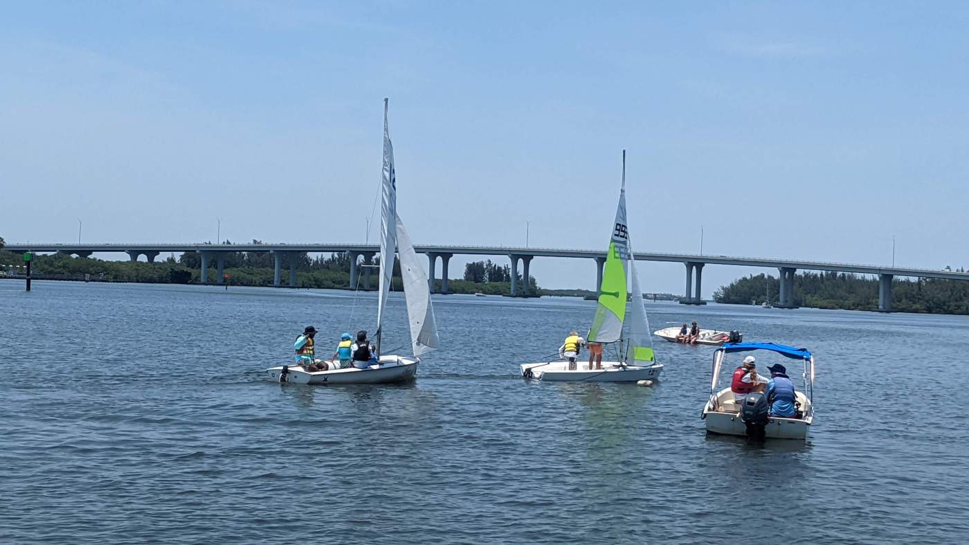 A group of sailboats sailing in the lagoon with a bridge in the background