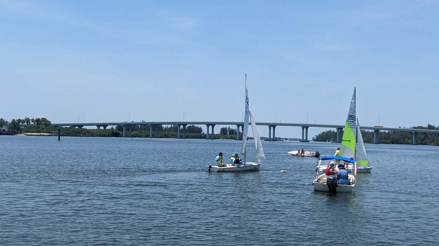 A group of sailboats sailing in the lagoon with a bridge in the background