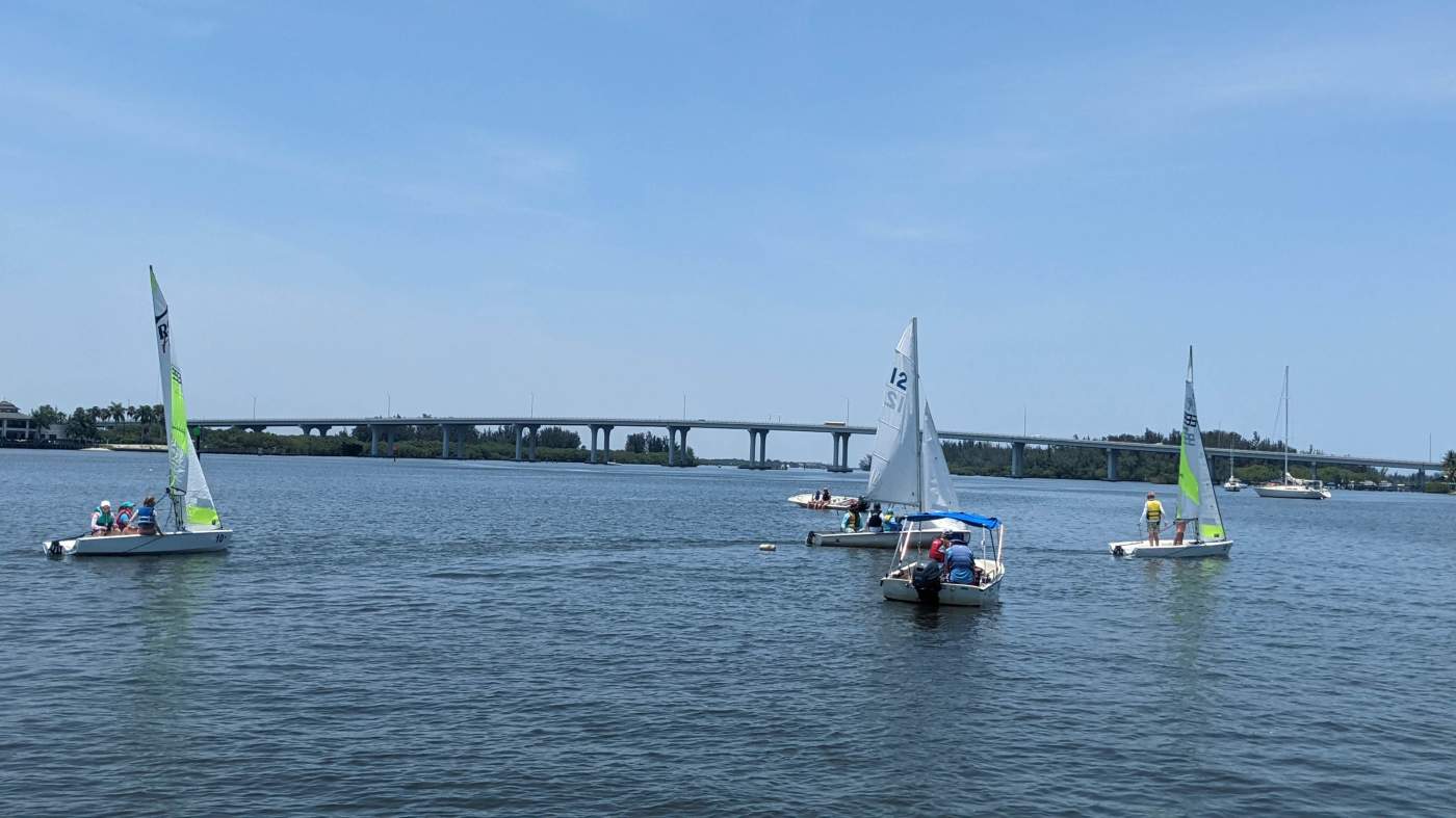 A group of sailboats sailing in the lagoon with a bridge in the background