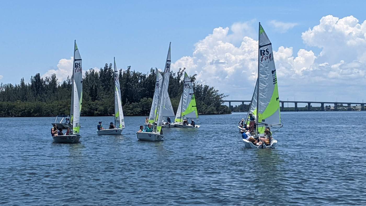 A group of sailboats sailing in the lagoon with a bridge in the background