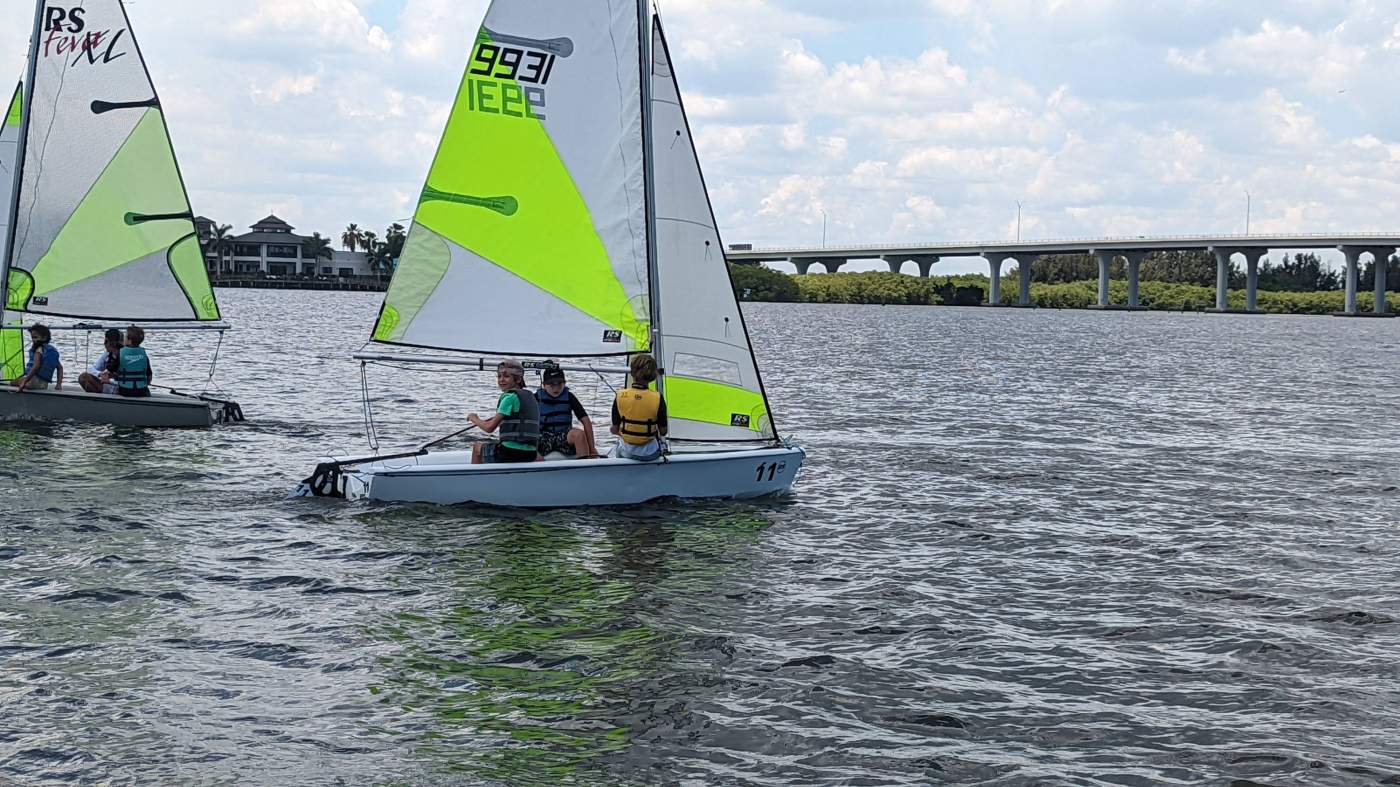 A group of sailboats sailing in the lagoon with a bridge in the background