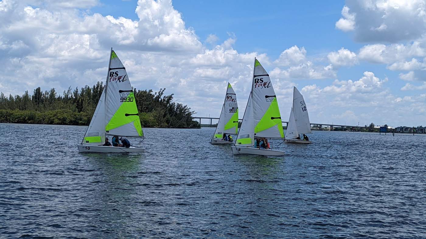 A group of sailboats sailing in the lagoon with a bridge in the background