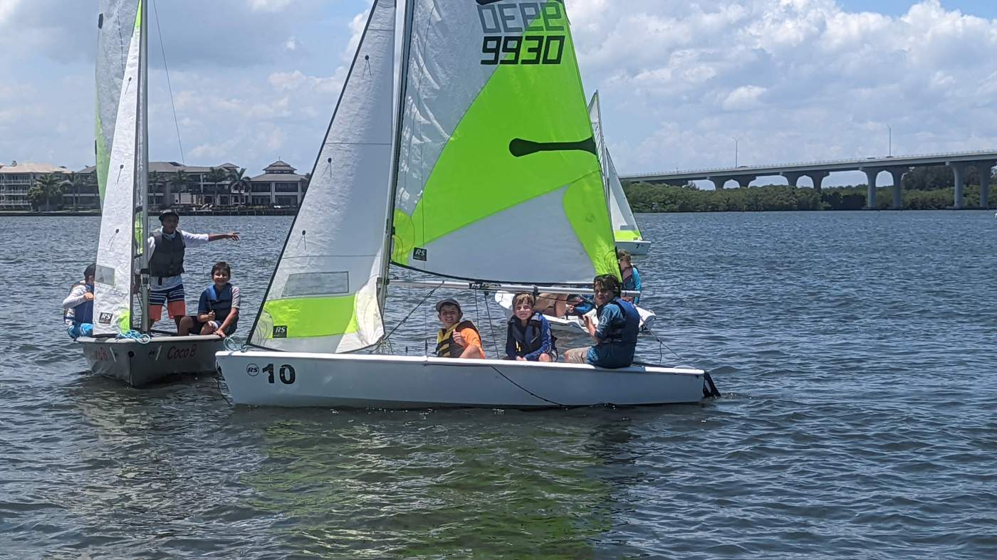 A group of sailboats sailing in the lagoon with a bridge in the background