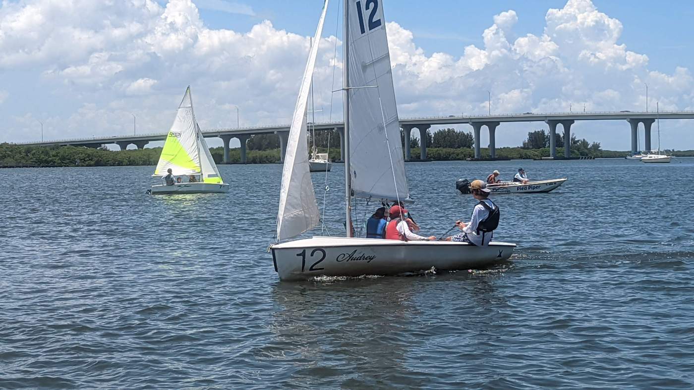 A group of sailboats sailing in the lagoon with a bridge in the background