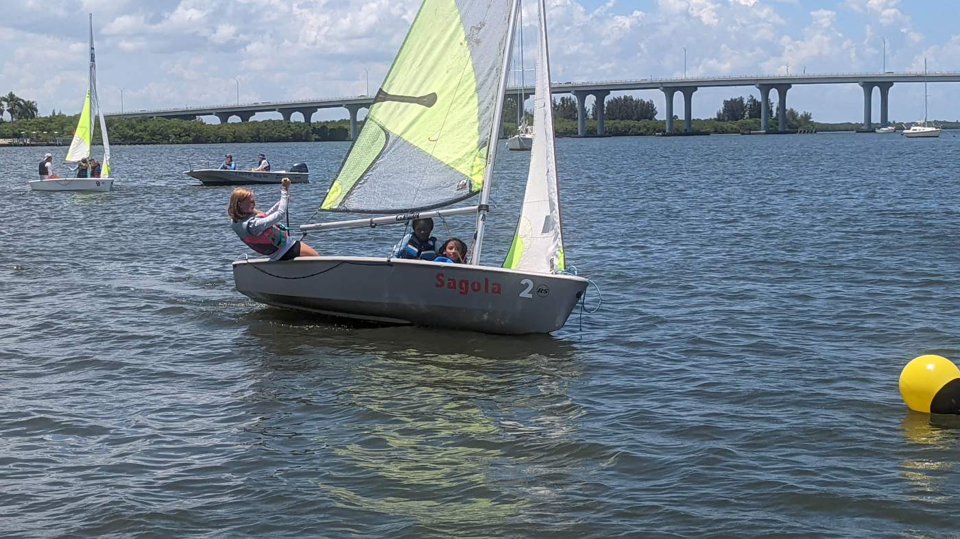 A group of sailboats sailing in the lagoon with a bridge in the background