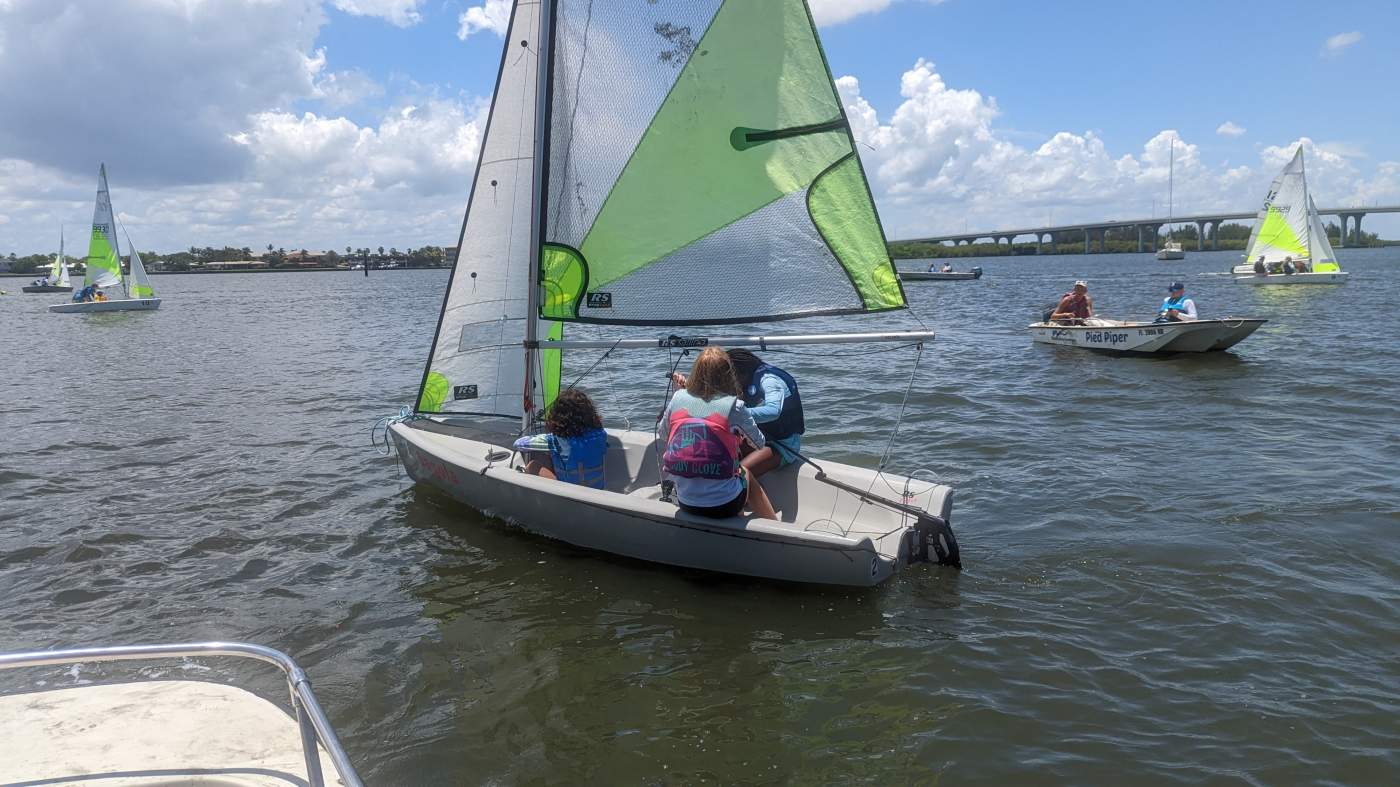 A group of sailboats sailing in the lagoon with a bridge in the background
