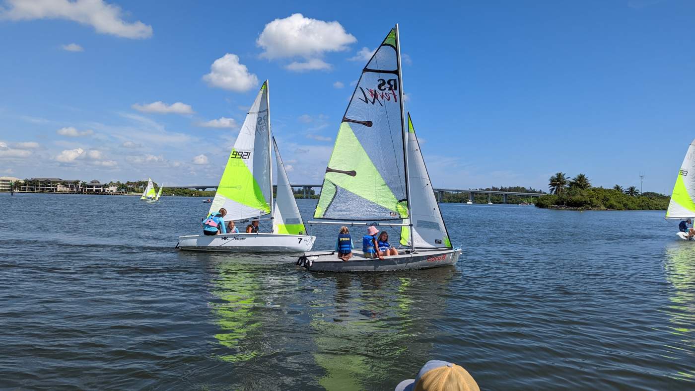 A group of sailboats sailing in the lagoon with a bridge in the background