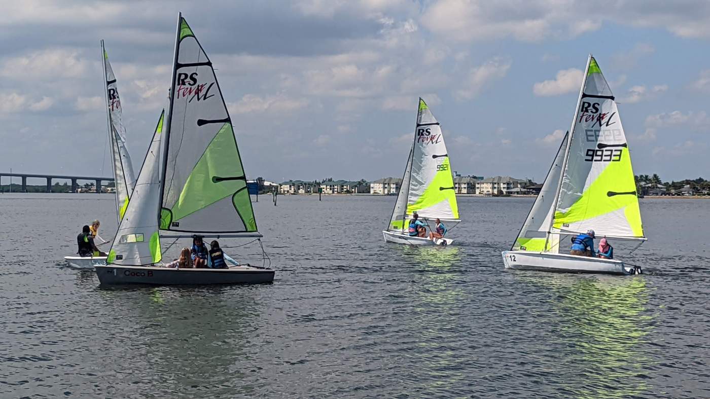 A group of sailboats sailing in the lagoon with a bridge in the background