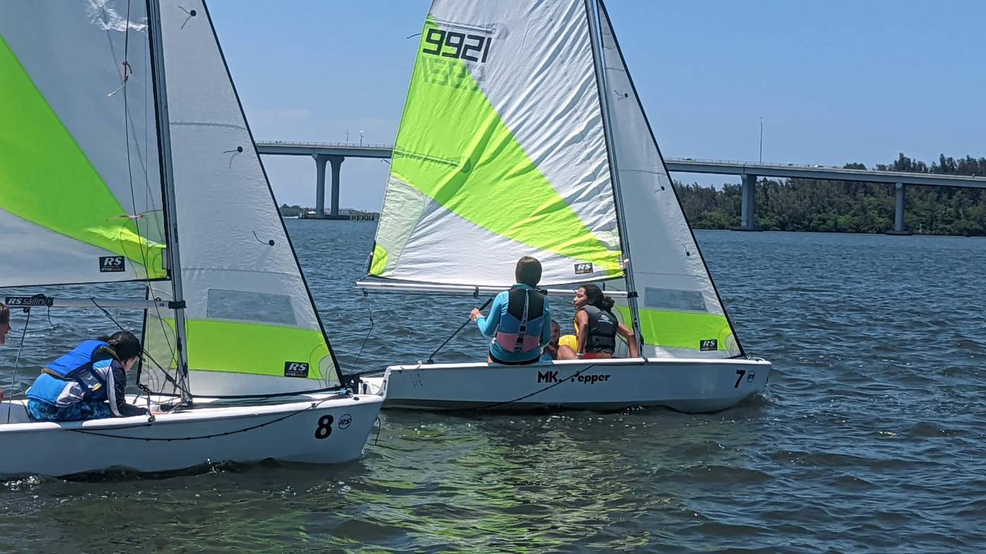 A group of sailboats sailing in the lagoon with a bridge in the background