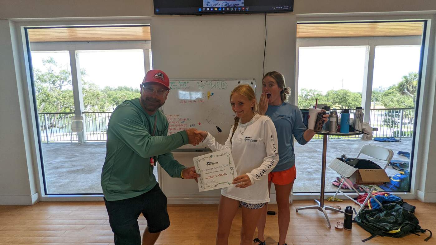 An instructor and several students standing in front of a whiteboard. One is receiving a certificate