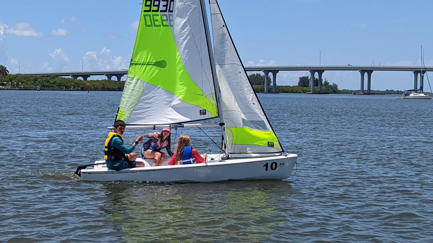 Children sailing a sailboat on the lagoon with a bridge in the background