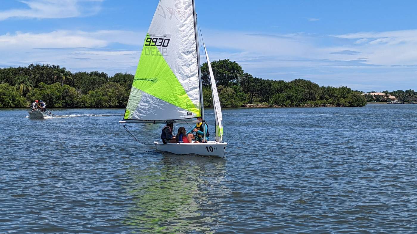 Children sailing followed by a powerboat