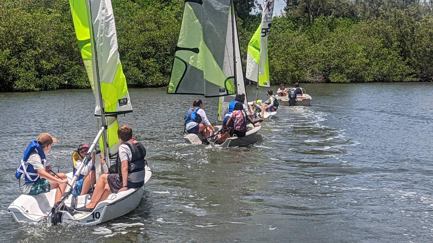 Three sailboats being towed by a powerboat