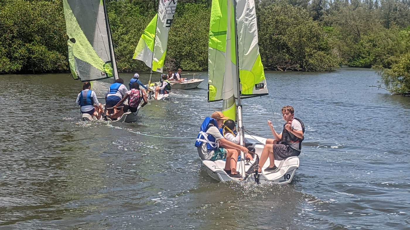 Three sailboats being towed by a powerboat