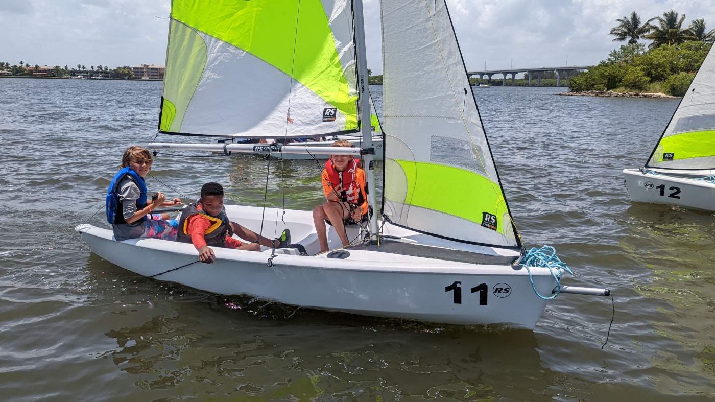 A group of sailboats sailing in the lagoon with a bridge in the background