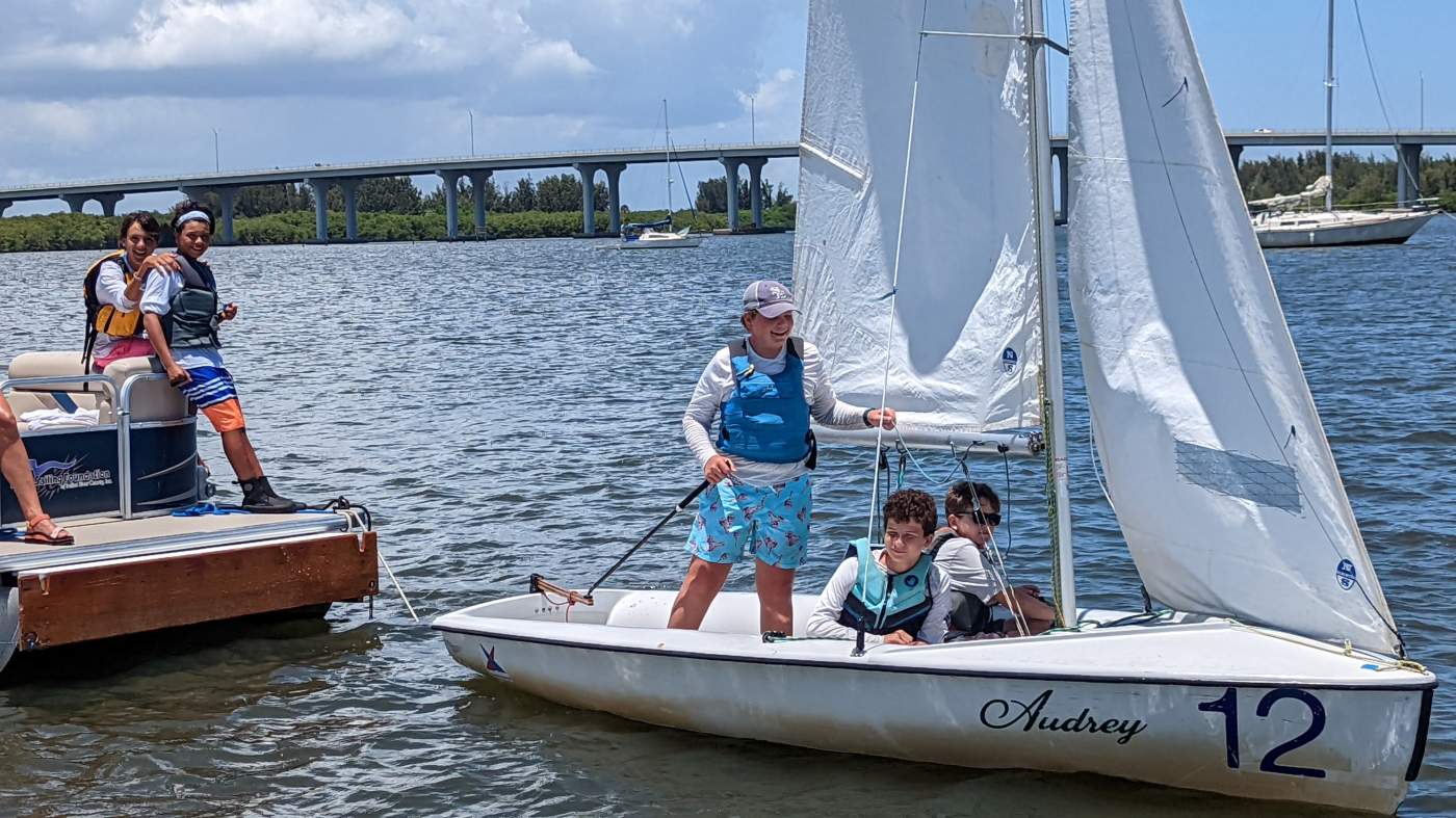 Children sailing a sailboat on the lagoon with a bridge in the background